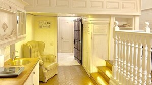 A hotel room with a herringbone floor, a sofa, a dining area with a sink, and a staircase with white balusters. - Apartment Fodorova 1 (Lviv)
