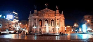 A historic building with classical architecture, a central fountain, and illuminated surroundings. - Apartment Svobody 10 (Lviv)