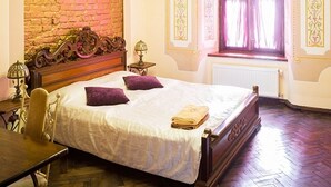Ein Schlafzimmer mit einem hölzernen Bett, zwei Kissen, einem Nachttisch mit Lampe, einem Stuhl, einem Fenster mit Vorhängen und einer Ziegelwand.