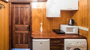 Eine kleine Küche mit Holztür, einem weißen Kühlschrank, einer Mikrowelle und einer Waschmaschine.