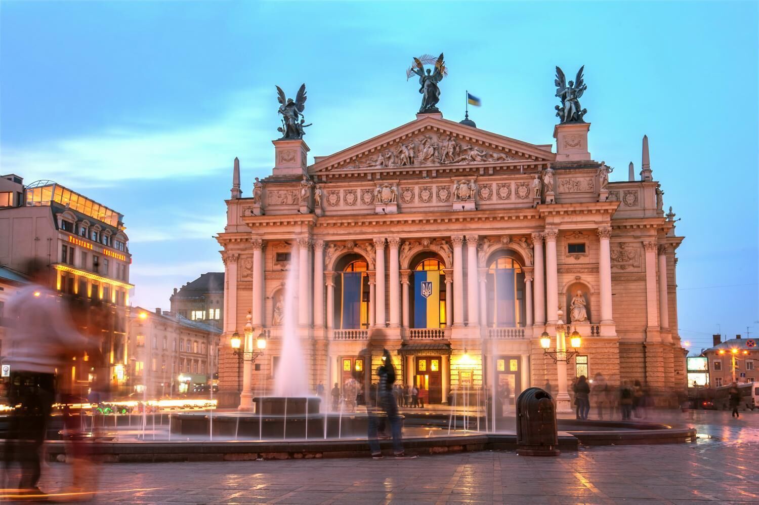 A grand building with classical architecture, featuring a central fountain and statues on the roof.