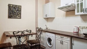 A compact kitchen with white cabinets, a washing machine, a coffee maker, and a decorative metal piece on the wall. - Apartment Virmenska 14 (Lviv)