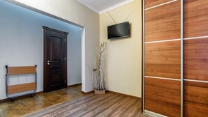 A hallway with a wooden floor, a dark door, a radiator, a television on the wall, and a wooden panel wall. - Apartment Virmenska 14 (Lviv)