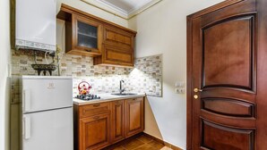 A compact kitchen with wooden cabinets, a white refrigerator, a gas stove, and a tiled backsplash. - Apartment Virmenska 14 (Lviv)