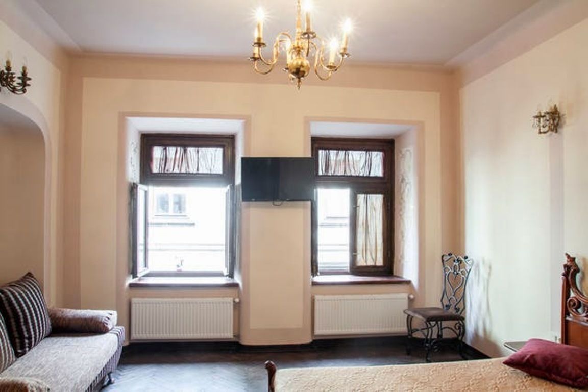 Quarto com cama, duas janelas, radiador, cadeira e lustre.