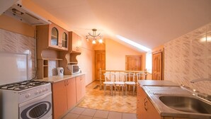A compact kitchen with a gas stove, oven, and microwave, wooden cabinets, a dining area with chairs, and a large window. - Economy Apartment Kopernika 9 (Lviv)