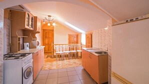 A compact kitchen with a gas stove, oven, microwave, and sink. There is a dining area with a table and chairs. - Economy Apartment Kopernika 9 (Lviv)
