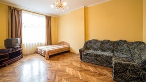 A room with a wooden herringbone floor, a sofa, a bed, a television on a stand, and a window with curtains. - Economy Apartment Kopernika 9 (Lviv)