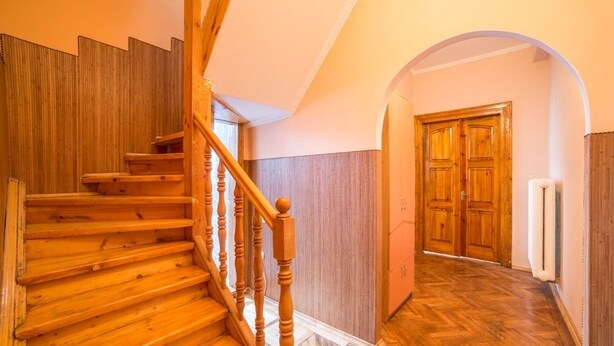 A wooden staircase with a handrail leading to a room with a wooden door and a radiator. - Economy Apartment Kopernika 9 (Lviv)