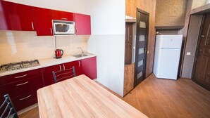 Una cocina pequeña con gabinetes rojos, un microondas, una estufa y un refrigerador.