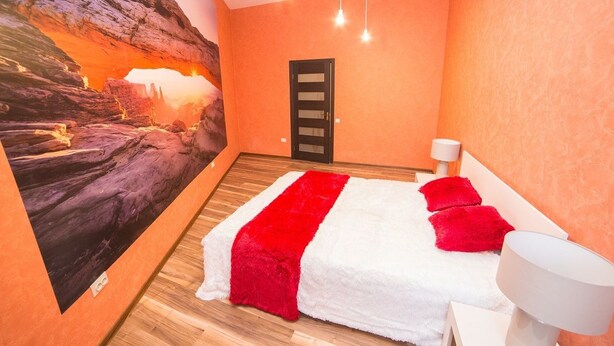 Un dormitorio con un amplio mural de un cañón, una cama con ropa de cama blanca y roja, piso de madera y una lámpara moderna.