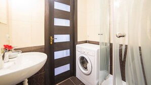 Un baño con lavamanos, lavadora y zona de ducha.