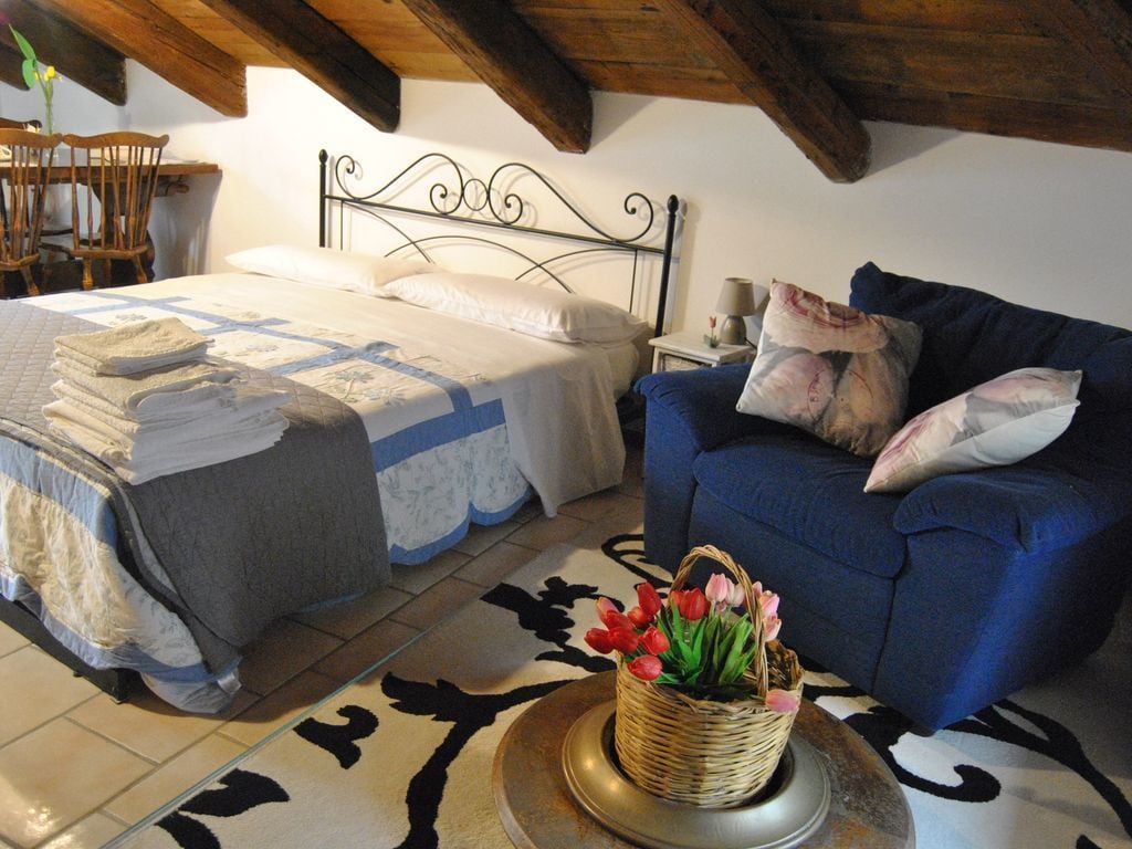Een slaapkamer met een bed, een blauwe bank, een rieten mand met bloemen en een kamerbreed tapijt met een patroon.
