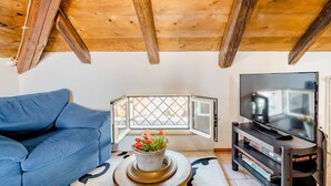 A cozy loft-style room with a blue sofa, a television, and a window with a view. - B&B Il Nido delle Rondini (Conversano)