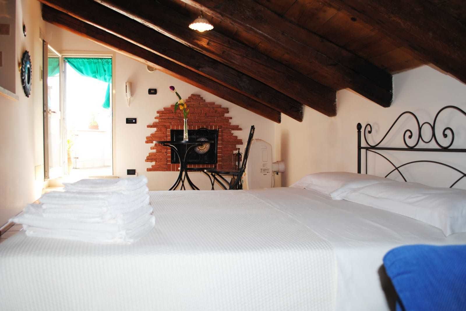 Een slaapkamer met een bed, een bakstenen openhaard, een tafel met stoel en een raam met gordijn.