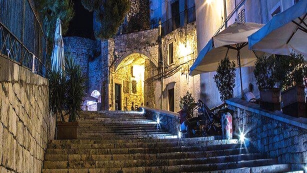 A stone staircase leading to a building with a lit entrance, surrounded by plants and umbrellas. - B&B Il Nido delle Rondini (Conversano)
