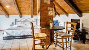 A cozy room with a bed, a small table with chairs, a TV, and a brick wall. - B&B Il Nido delle Rondini (Conversano)