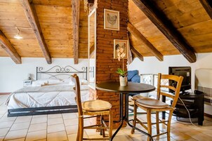 Una habitación acogedora con una cama, una mesita con sillas, un televisor y una pared de ladrillo.