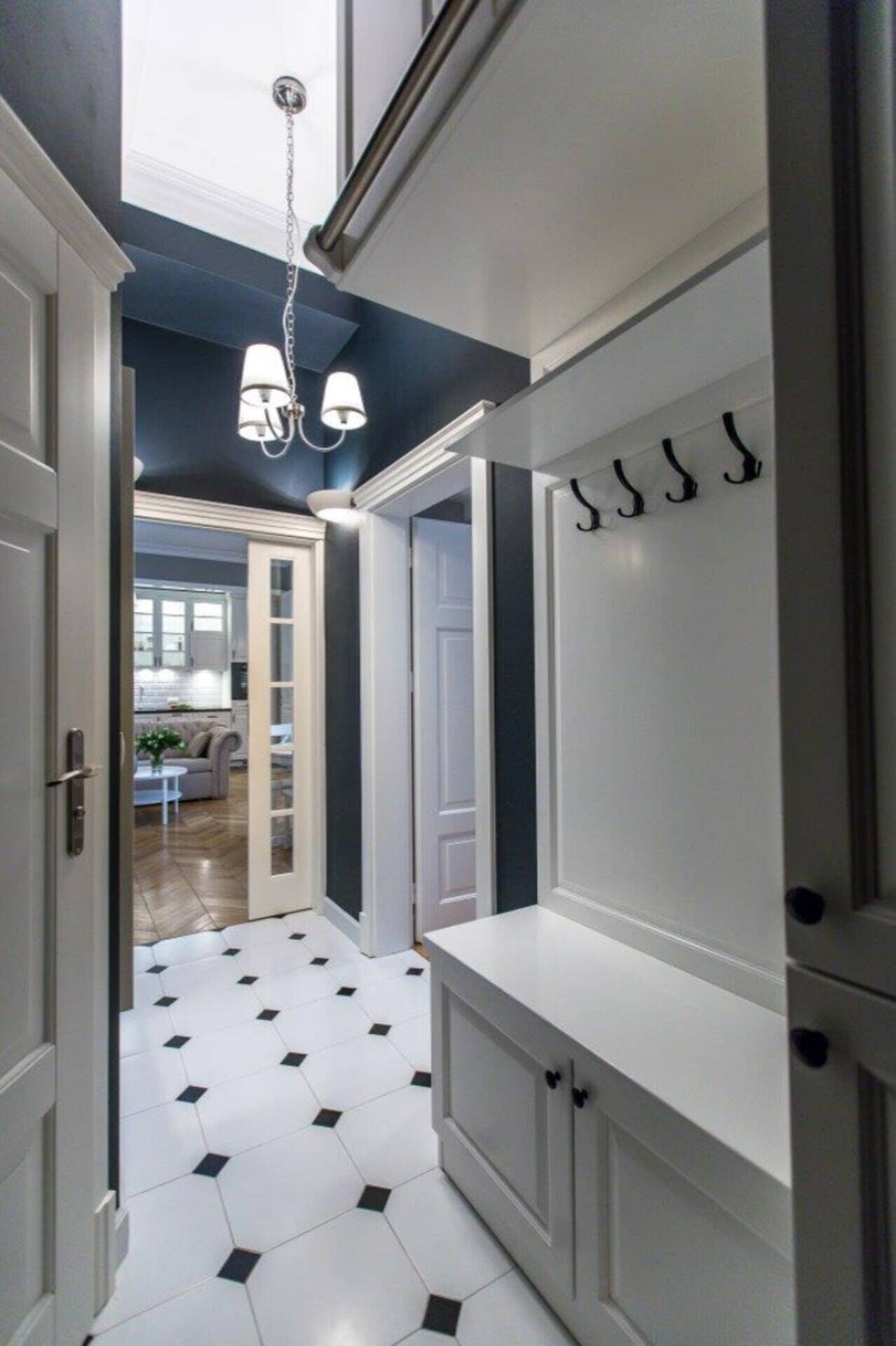 A hallway with a white bench, black and white tiled floor, and a ceiling light fixture.