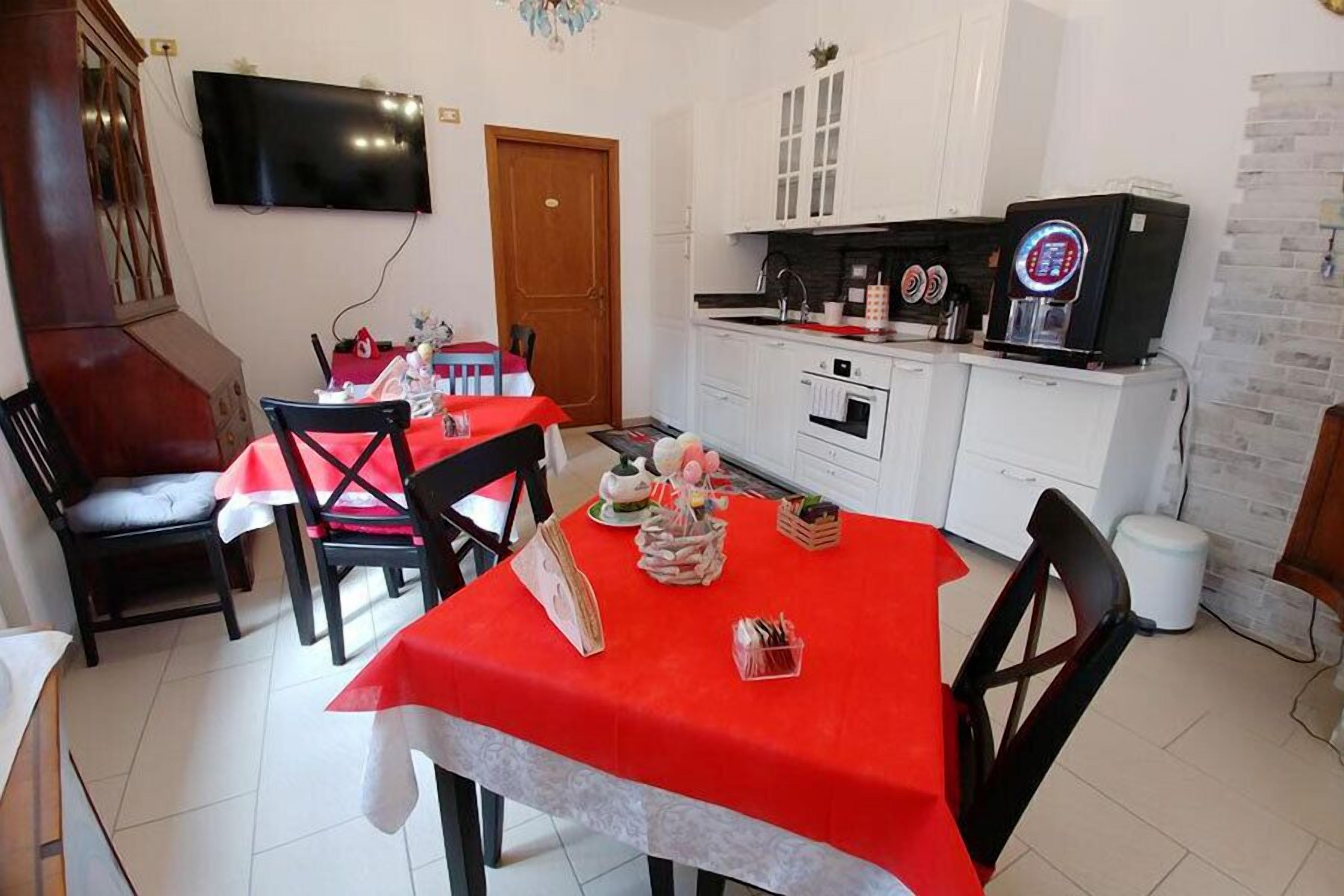 A dining area with a red tablecloth, white cabinets, a TV mounted on the wall, and a kitchen area with appliances.