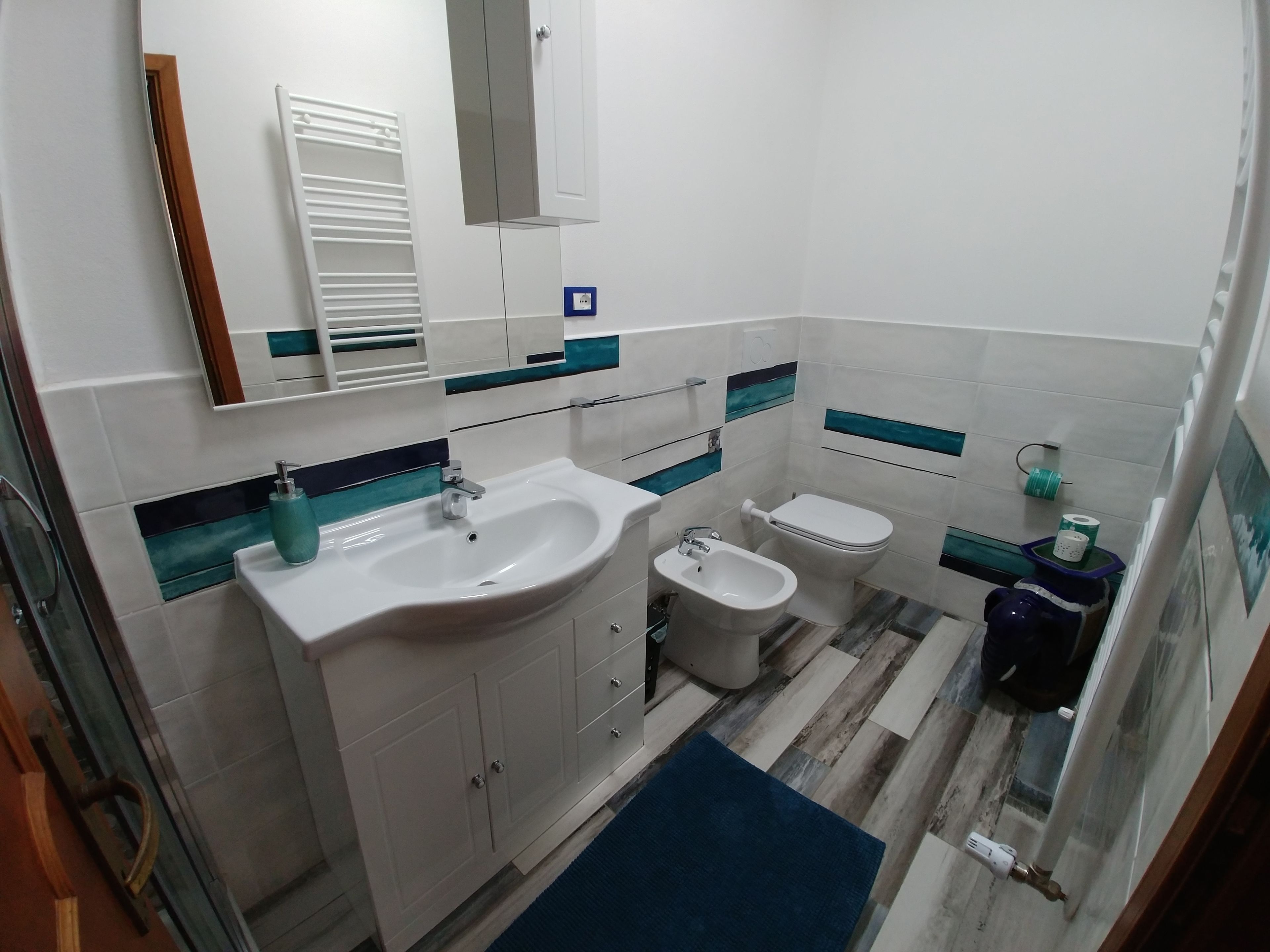 A modern bathroom with a white sink, bidet, and toilet. There is a mirror above the sink and a cabinet below it.