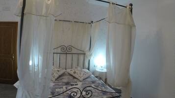 A four-poster bed with a metal frame and a patterned bedspread, surrounded by sheer white curtains.
