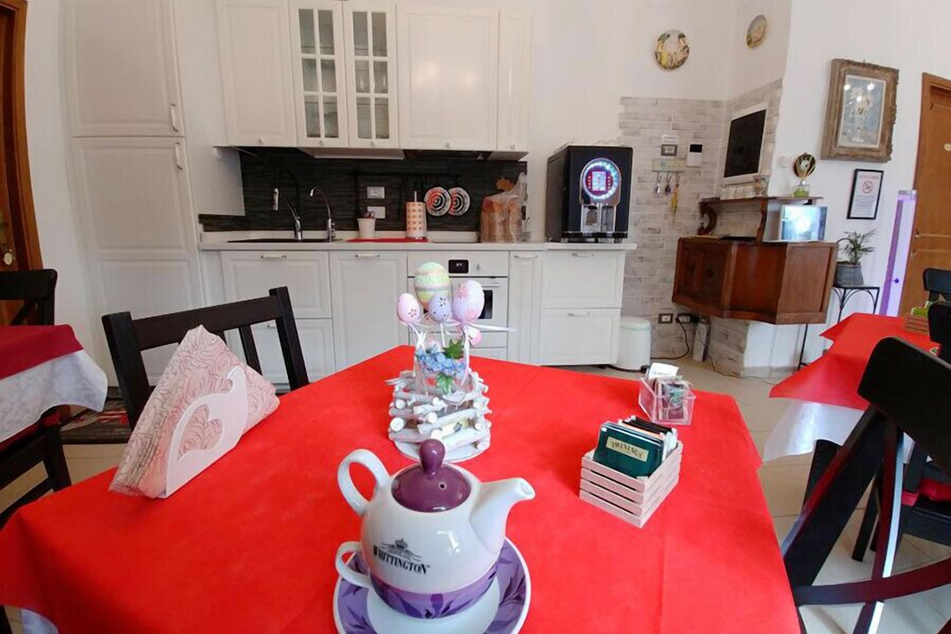 A dining area with a red tablecloth, a white teapot, and a small bookshelf.