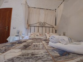 Un dormitorio con cama, una puerta de madera, una mesita de noche y un ventanal con cortinas.