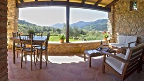 Un patio con pareti in pietra, un tavolo e sedie, un divano e vista su un paesaggio montuoso.