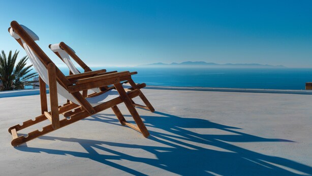 A wooden lounge chair with a white cushion, positioned on a white surface with a clear view of the ocean and distant mountains. - Als Mansion by K&K (Oia)