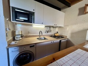 A compact kitchen with a microwave, coffee maker, sink, stove, and a washing machine. - Charming 2-Room Apartment with Golf View, Terrace, A/C, Parking - 1300m from Beach (Saint-Cyprien)