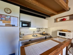 A compact kitchen with a microwave, stove, sink, and a clock on the wall.
