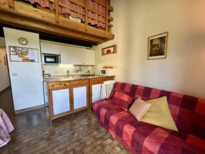 Um espaço de estar compacto com cozinha compacta, um sofá e um mezanino com toalha de mesa xadrez.