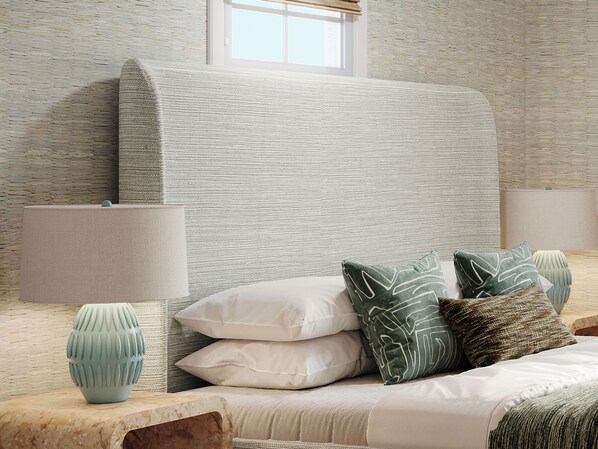 A neatly arranged bedroom with a bed, pillows, a vase, and a lamp.