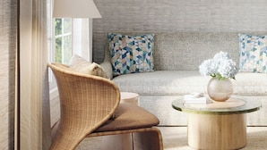 A modern living room with a wicker chair, a round coffee table with a vase, and a sofa with patterned cushions. -  Shore Haven Inn (Falmouth)