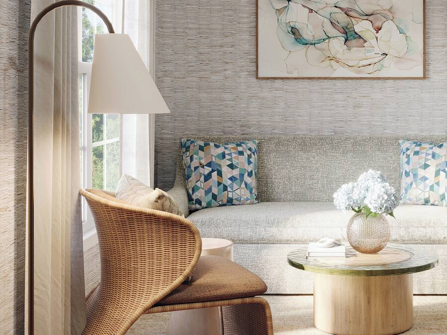 Een moderne woonkamer met een rieten fauteuil, een ronde salontafel met een vaas en een bank met decoratieve kussens.