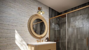 A modern bathroom with a wooden vanity, a round mirror, and a glass shower enclosure. -  Shore Haven Inn (Falmouth)