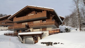 A multi-story wooden chalet with balconies, set in a snowy landscape. - 3-room apartment with balcony and garage near the slopes (La Clusaz)