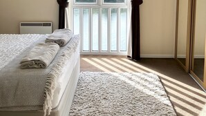 Quarto com cama, radiador, janela grande com cortinas e vista para árvores.