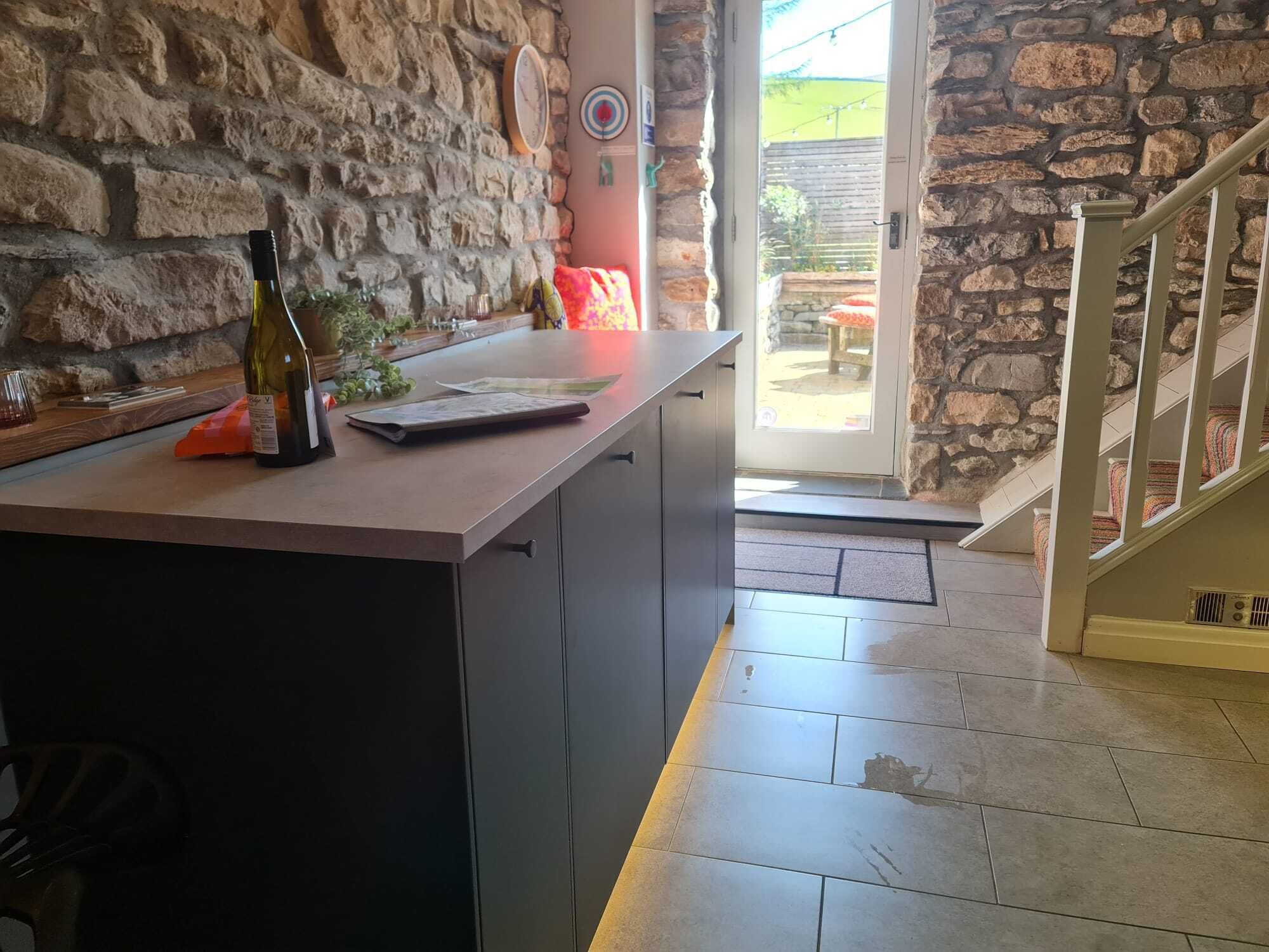 Une cuisine avec un mur en pierre, un comptoir en bois et une porte donnant sur l’extérieur.