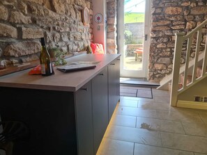 A kitchen with a stone wall, a wooden counter, and a door leading outside.