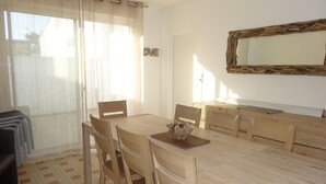 A dining area with a wooden table and chairs, a mirror on the wall, and a window with sheer curtains.