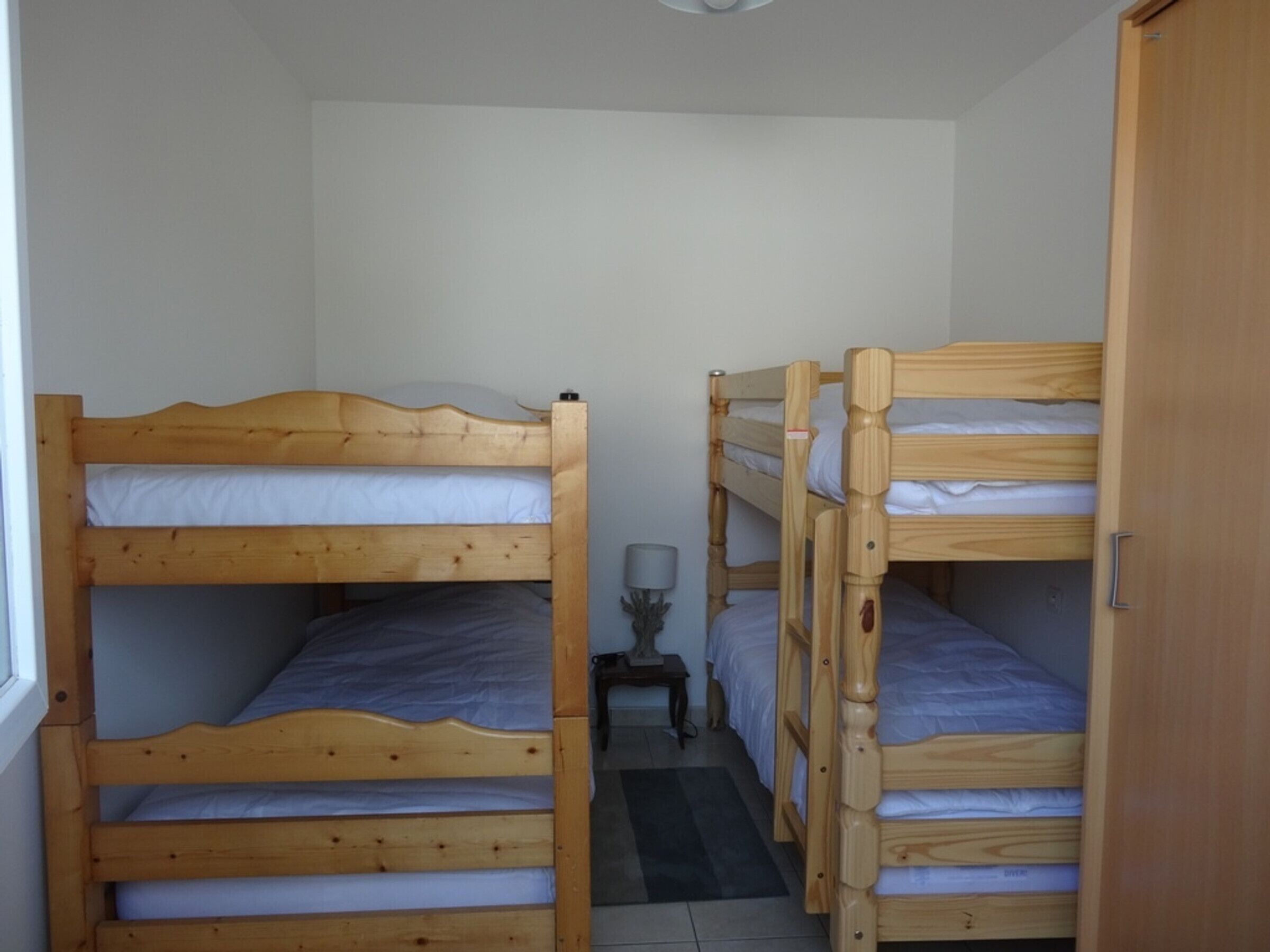 A room with three bunk beds, a small table with a lamp, and a window.