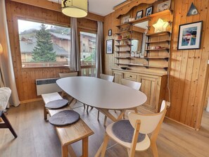 A cozy room with a wooden interior, a round table with chairs, and a window with a view of houses and trees.