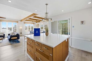 A spacious kitchen with wooden cabinets, a central island, and a large window providing a view. - It's All Good | 780 ft from the beach | Private Pool, Dog Friendly, Hot Tub (Virginia Beach)