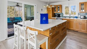 A modern kitchen with a large island, wooden cabinets, and a view to an outdoor patio. - It's All Good | 780 ft from the beach | Private Pool, Dog Friendly, Hot Tub (Virginia Beach)