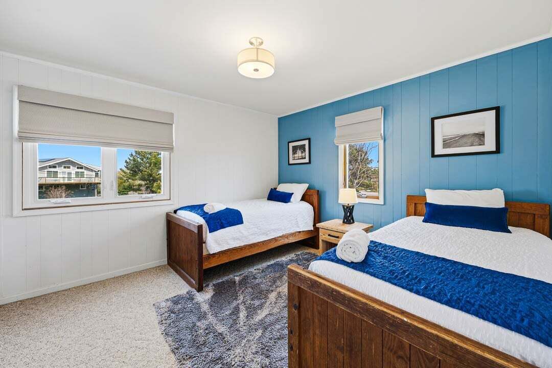 Une chambre avec deux lits, une fenêtre donnant sur un beau paysage, un luminaire au plafond et un tableau encadré au mur.