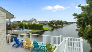 A deck with Adirondack chairs overlooking a river, a pool, and a view of houses across the water. - It's All Good | 780 ft from the beach | Private Pool, Dog Friendly, Hot Tub (Virginia Beach)