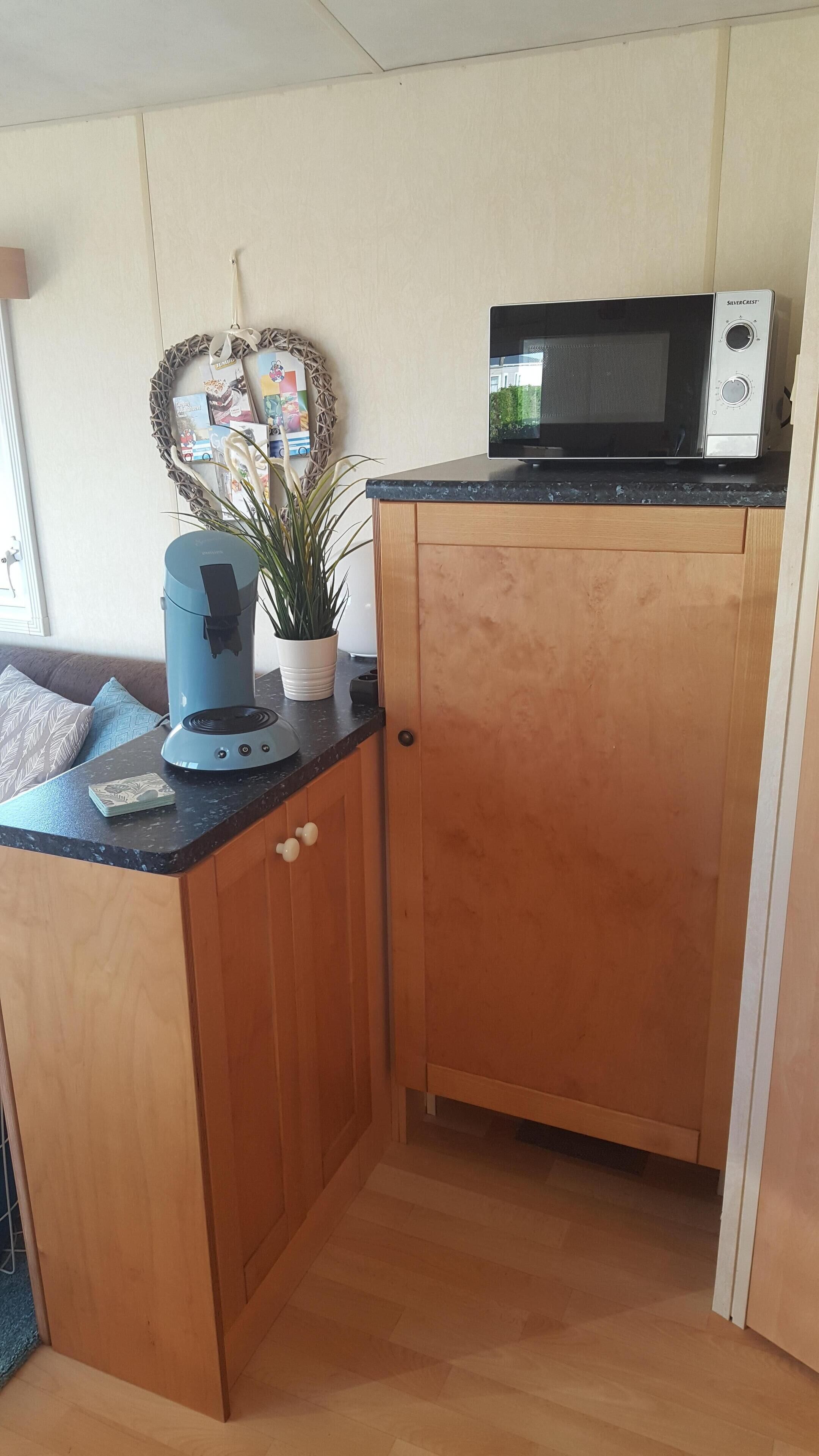 Une cuisine compacte équipée d’un four à micro-ondes, d’une machine à café et d’une plante en pot posée sur le plan de travail.