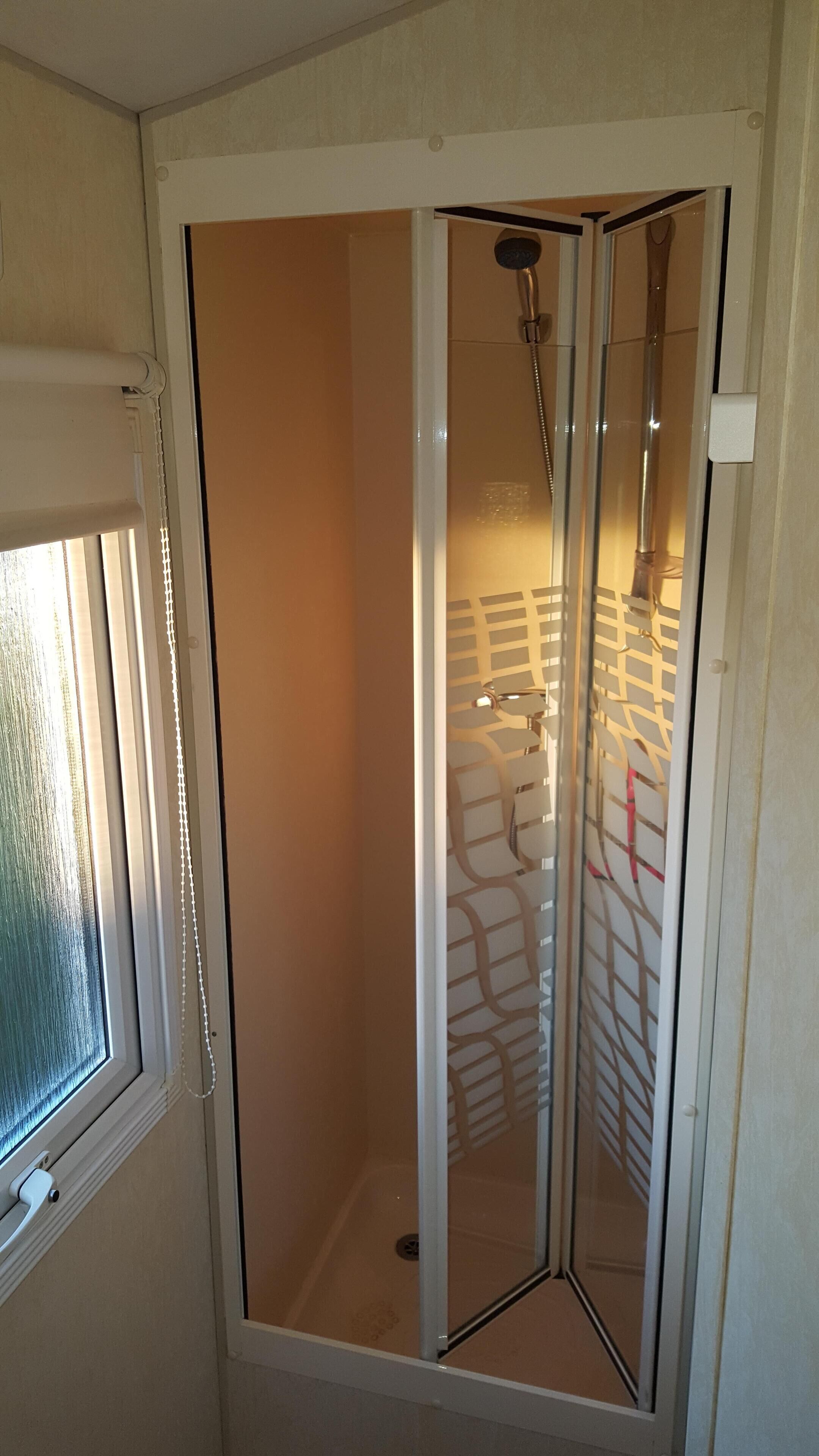 Une cabine de douche fermée par des parois en verre, équipée d’un pommeau de douche et d’un porte-serviettes.